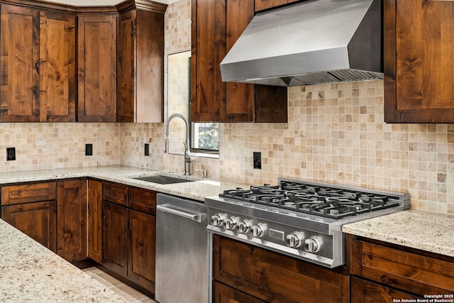 kitchen featuring light stone counters, a sink, wall chimney range hood, and stainless steel gas stovetop