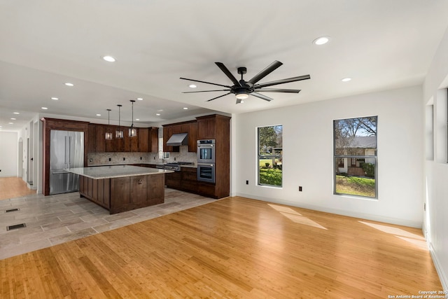 kitchen with a kitchen island, decorative backsplash, light countertops, appliances with stainless steel finishes, and open floor plan