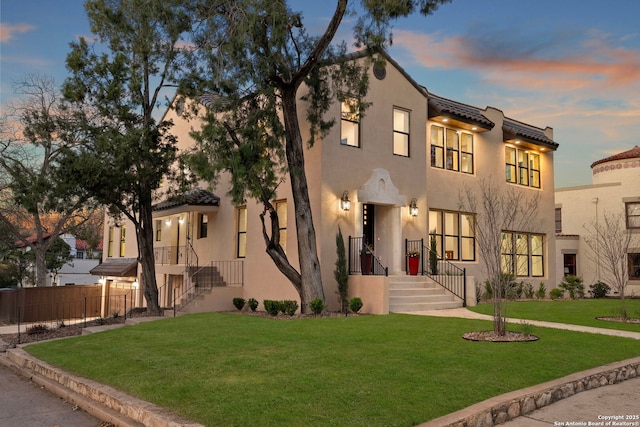 view of front of house with a front yard, fence, a tile roof, and stucco siding