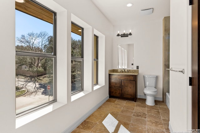 full bath featuring toilet, stone finish flooring, a shower, baseboards, and vanity