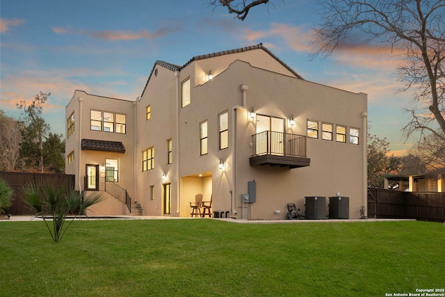 rear view of house with a balcony, a yard, fence, and stucco siding