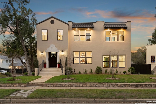 view of front of house featuring stucco siding, fence, a front yard, and a tile roof