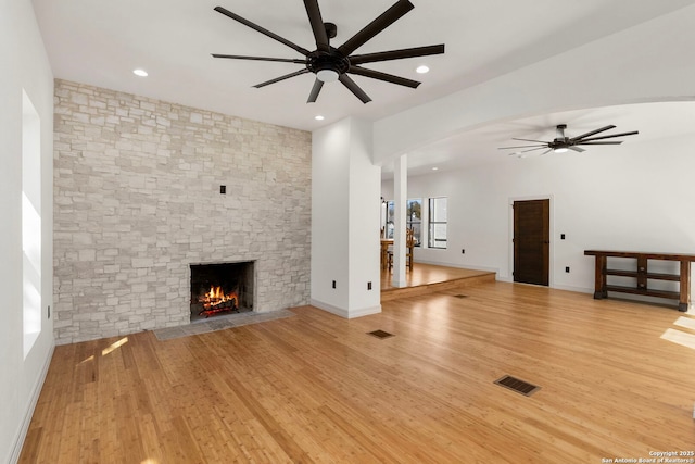 unfurnished living room featuring light wood finished floors, visible vents, a stone fireplace, and a ceiling fan