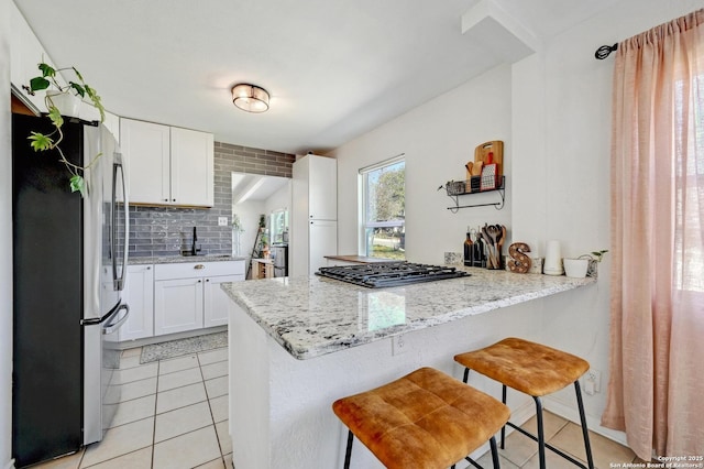 kitchen featuring tasteful backsplash, white cabinetry, freestanding refrigerator, a peninsula, and light tile patterned flooring