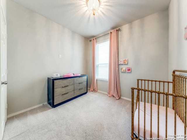 bedroom featuring baseboards, a crib, and carpet flooring