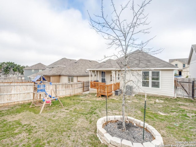 rear view of property featuring a deck, a lawn, a fenced backyard, and a playground