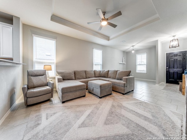 living room with baseboards, a tray ceiling, and ornamental molding