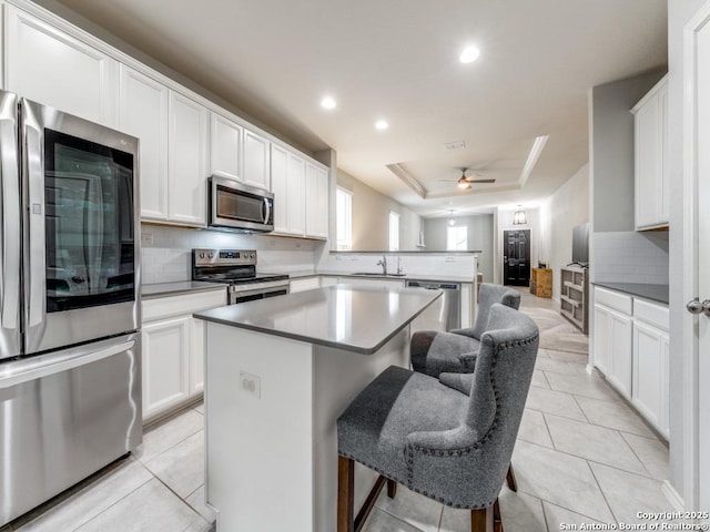 kitchen featuring a tray ceiling, a kitchen island, stainless steel appliances, a peninsula, and light tile patterned floors