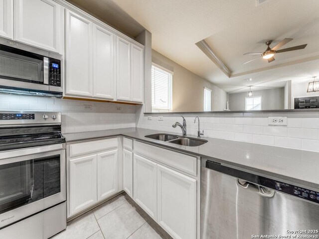 kitchen with light tile patterned floors, a tray ceiling, a sink, stainless steel appliances, and tasteful backsplash