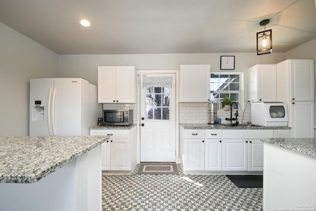 kitchen with light stone countertops, a sink, white fridge with ice dispenser, white cabinetry, and stainless steel microwave