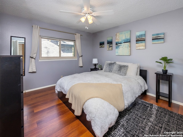 bedroom with a ceiling fan, wood finished floors, baseboards, and a textured ceiling