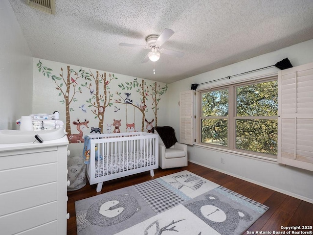 bedroom featuring baseboards, visible vents, hardwood / wood-style flooring, a nursery area, and a textured ceiling