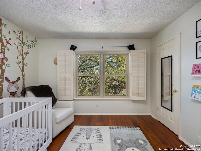 bedroom with a nursery area, a textured ceiling, baseboards, and wood finished floors