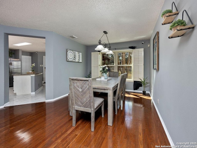 dining space featuring a textured ceiling, wood finished floors, visible vents, and baseboards