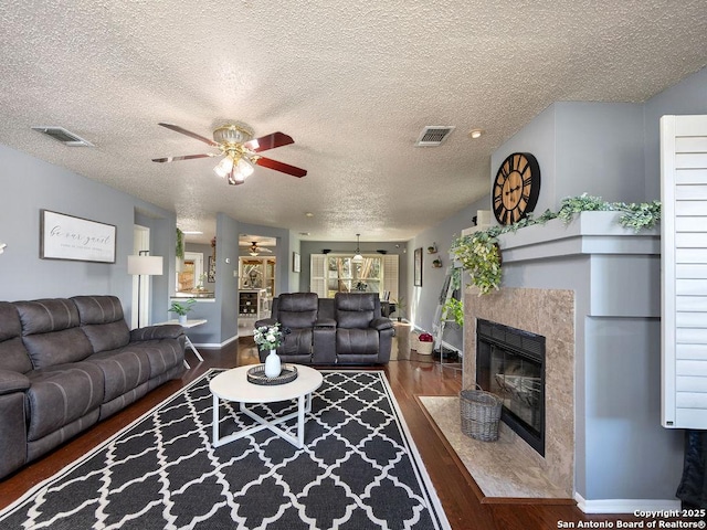 living area featuring a premium fireplace, visible vents, wood finished floors, and a ceiling fan