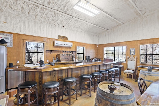 bar with a community bar, finished concrete flooring, a wall mounted AC, and freestanding refrigerator