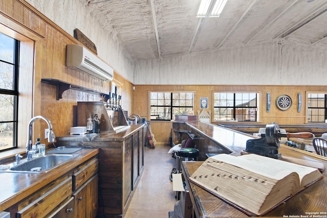 kitchen with a wall mounted AC, a sink, dark countertops, concrete floors, and brown cabinetry