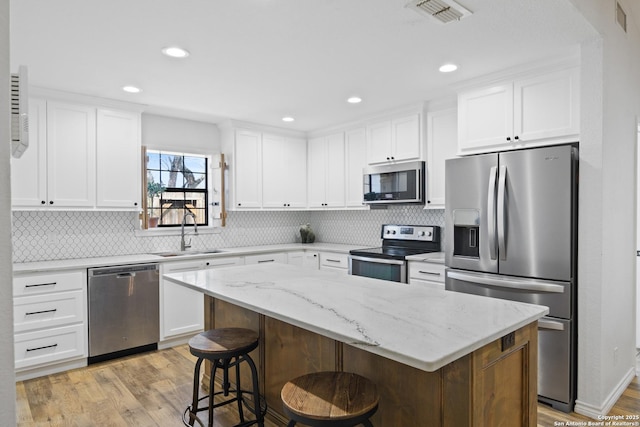 kitchen featuring visible vents, a sink, stainless steel appliances, light wood-style floors, and white cabinetry