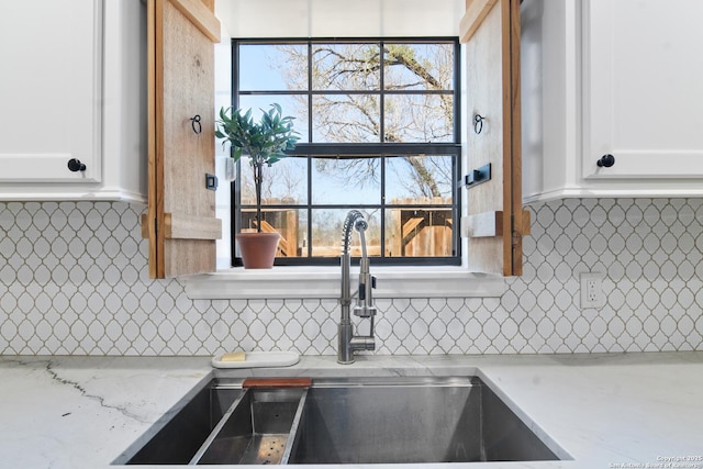 kitchen with white cabinets, light stone countertops, backsplash, and a sink