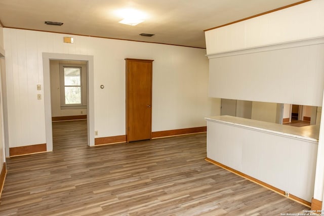 empty room featuring visible vents, ornamental molding, baseboards, and wood finished floors