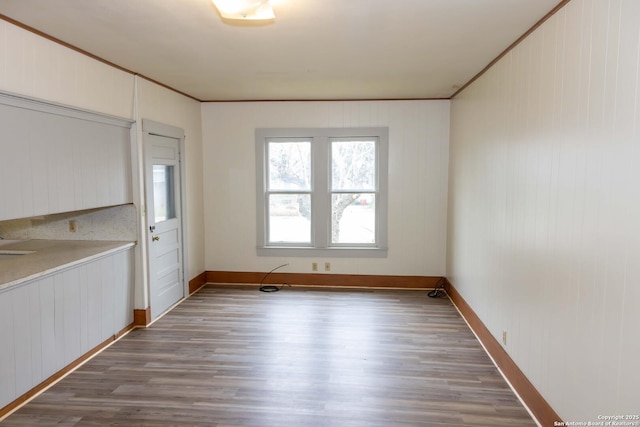 unfurnished dining area with ornamental molding, baseboards, and wood finished floors