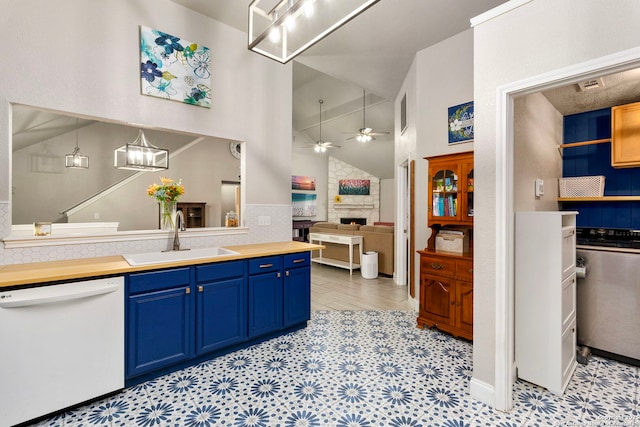 kitchen with ceiling fan, a fireplace, white dishwasher, blue cabinets, and a sink