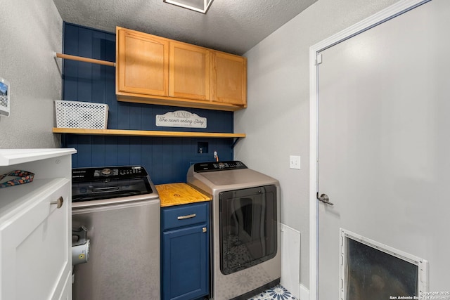 laundry room with washing machine and clothes dryer, cabinet space, and a textured ceiling