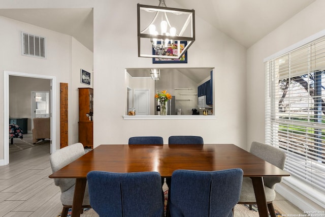 dining area with visible vents, high vaulted ceiling, an inviting chandelier, and wood finished floors