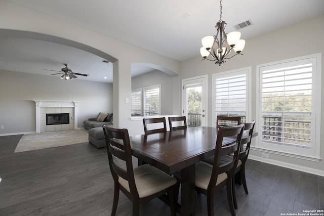 dining area with visible vents, baseboards, a tiled fireplace, dark wood finished floors, and ceiling fan with notable chandelier