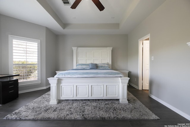 bedroom with a ceiling fan, dark wood-style floors, baseboards, visible vents, and a tray ceiling