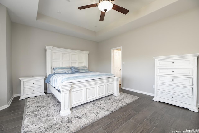 bedroom with a tray ceiling, baseboards, ceiling fan, and dark wood-style flooring