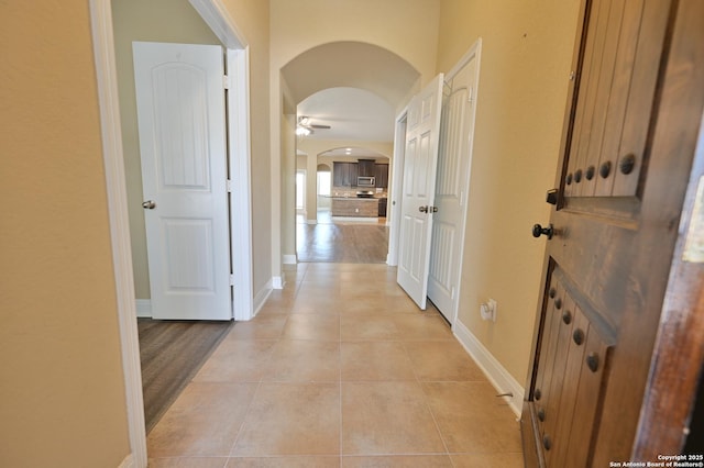 hallway featuring arched walkways, light tile patterned floors, and baseboards