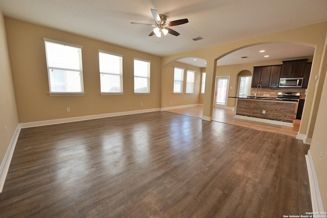 unfurnished living room with a ceiling fan, visible vents, baseboards, and dark wood-style flooring