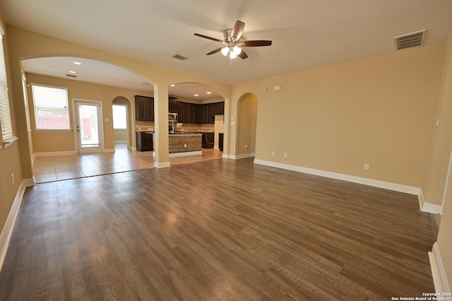 unfurnished living room with dark wood-type flooring, arched walkways, visible vents, and ceiling fan