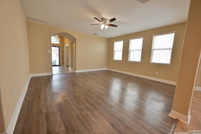 empty room featuring visible vents, arched walkways, a healthy amount of sunlight, and wood finished floors