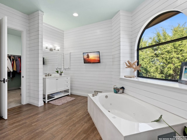 bathroom with a walk in closet, a whirlpool tub, wood finished floors, and vanity