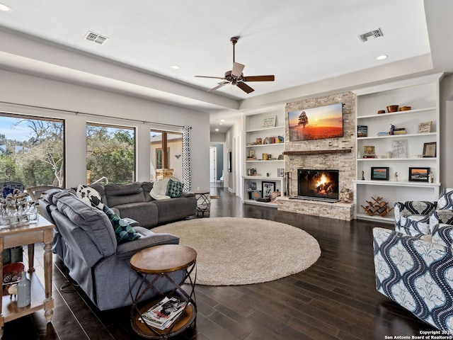 living room featuring built in features, visible vents, a stone fireplace, and dark wood finished floors