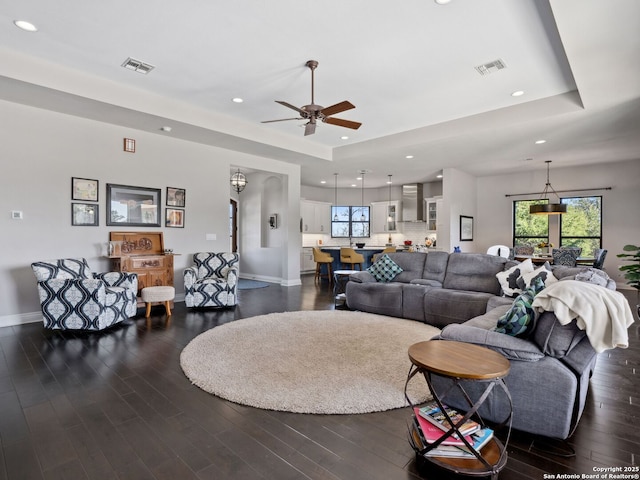 living room featuring a tray ceiling, visible vents, and dark wood-style flooring