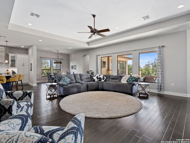 living room featuring baseboards, visible vents, recessed lighting, dark wood-type flooring, and a raised ceiling