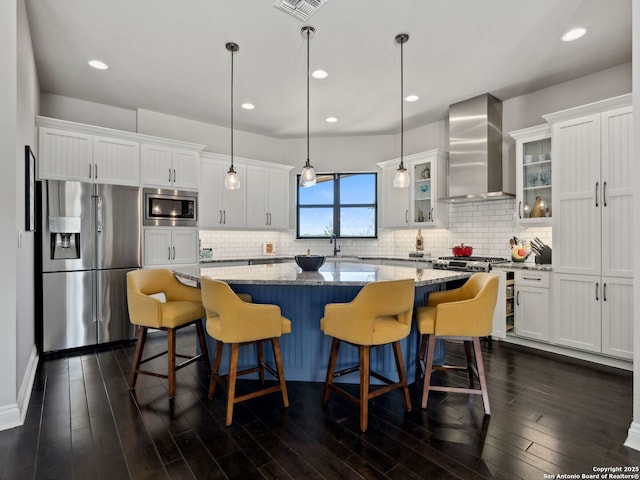 kitchen featuring stainless steel appliances, wall chimney exhaust hood, a center island, and white cabinets