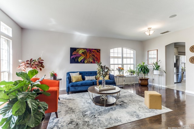 living room featuring wood finished floors, arched walkways, visible vents, and baseboards