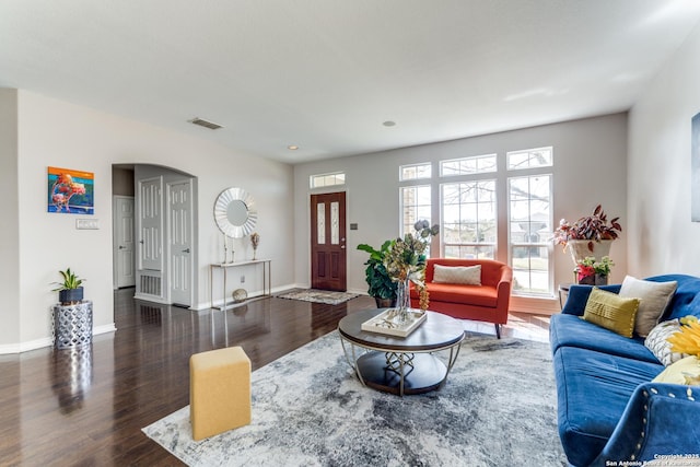 living area with baseboards, arched walkways, visible vents, and wood finished floors