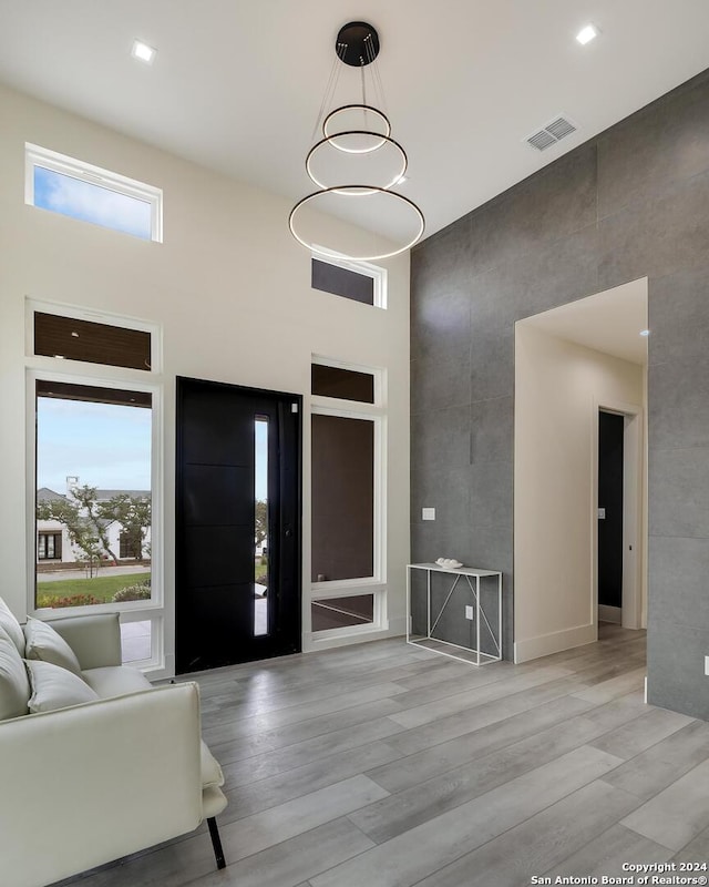 foyer featuring a wealth of natural light, visible vents, light wood-style flooring, and a towering ceiling