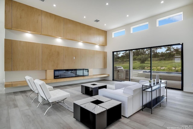 living room featuring light wood finished floors, a glass covered fireplace, a high ceiling, and visible vents