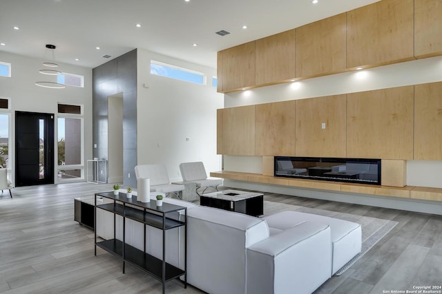 living area featuring light wood finished floors, visible vents, recessed lighting, and a towering ceiling