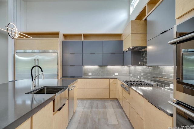 kitchen with modern cabinets, wall chimney range hood, light brown cabinets, and stainless steel appliances