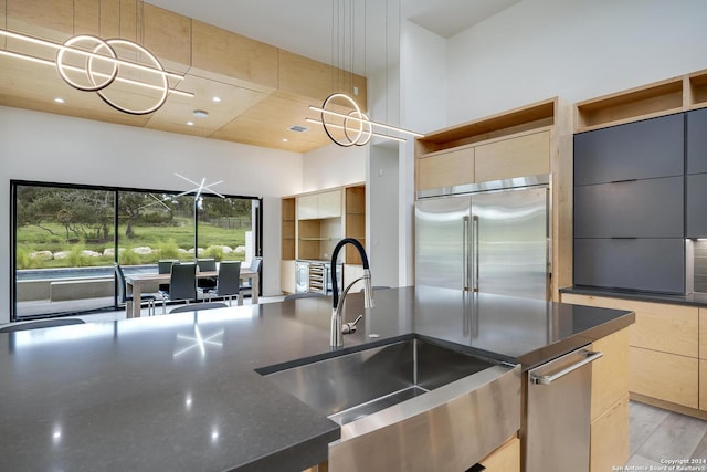 kitchen with dark stone counters, a sink, a towering ceiling, built in fridge, and modern cabinets