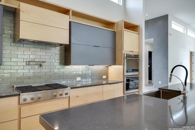 kitchen with dark countertops, tasteful backsplash, appliances with stainless steel finishes, a towering ceiling, and a sink