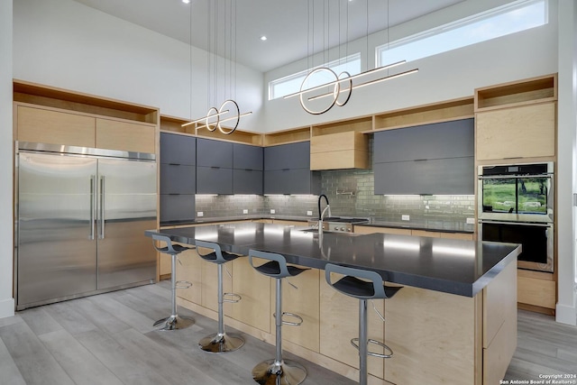 kitchen featuring light wood finished floors, a high ceiling, stainless steel appliances, modern cabinets, and a sink