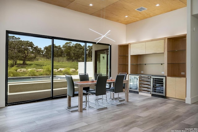 dining area with beverage cooler, visible vents, light wood-style flooring, wood ceiling, and a towering ceiling